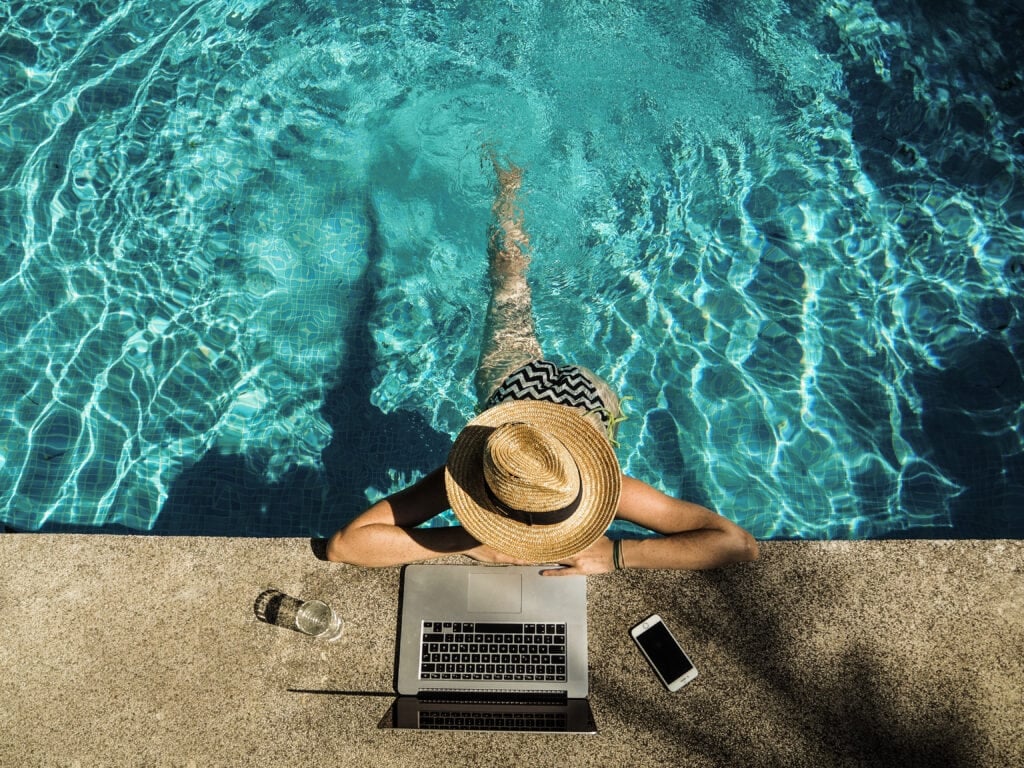 woman working from pool on a laptop as a travel agent