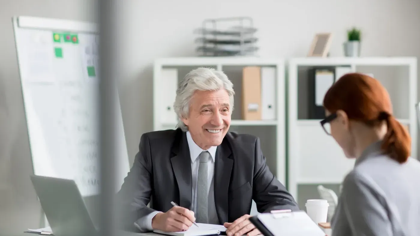 A man smiling at a woman whilst writing on a sheet of paper with a pen