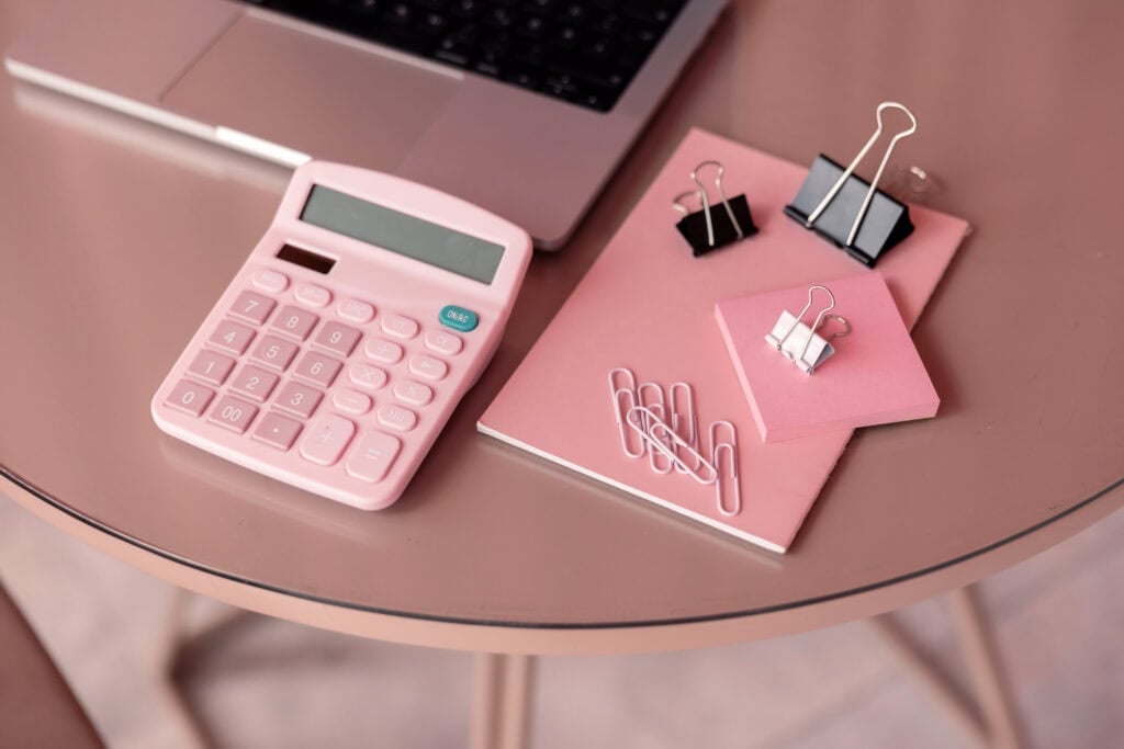 pink calculator on desk with notepad and clips