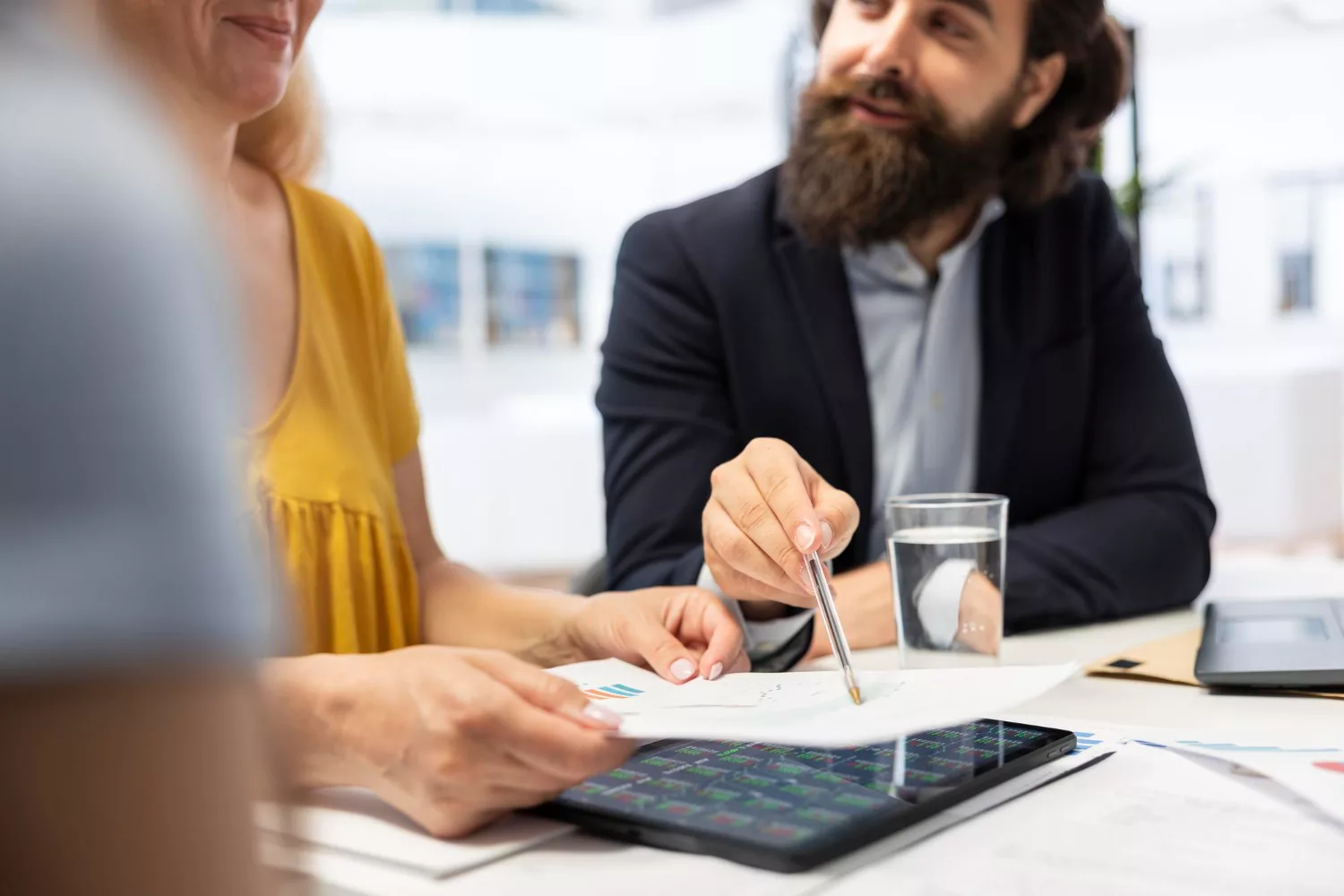 Two professionals discussing documents and graphs related to business insurance cost for startups at a meeting table.